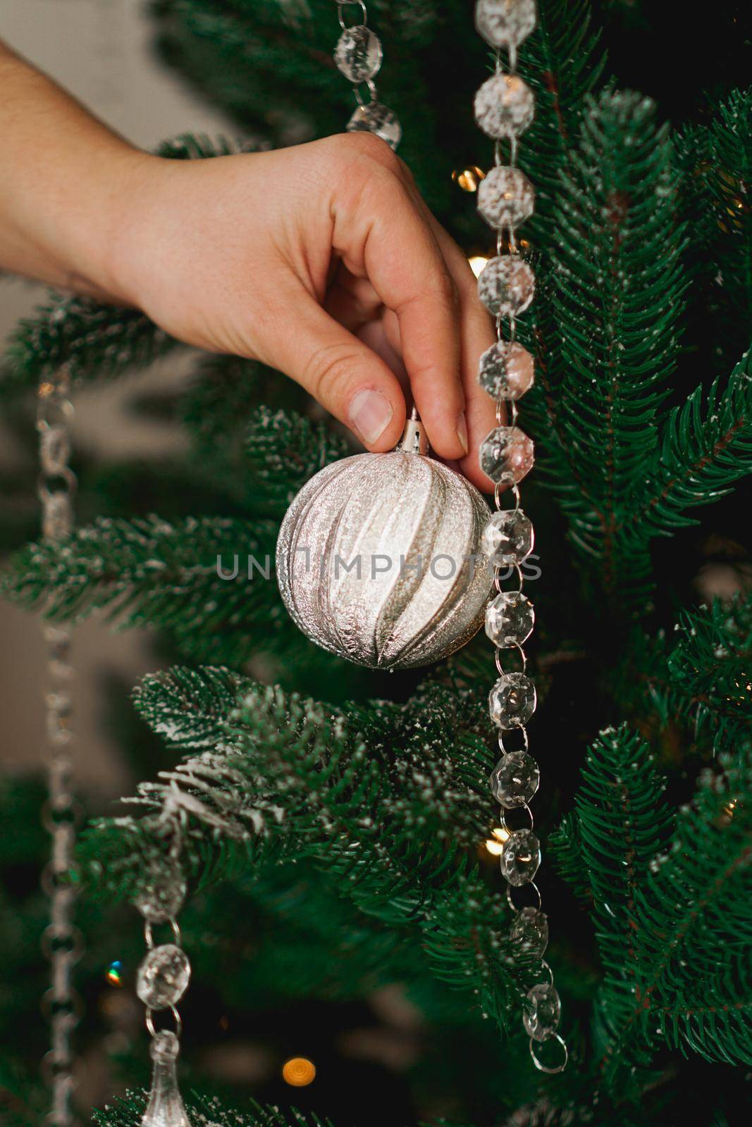 Female hands decorating green christmas tree with a silver balls.
