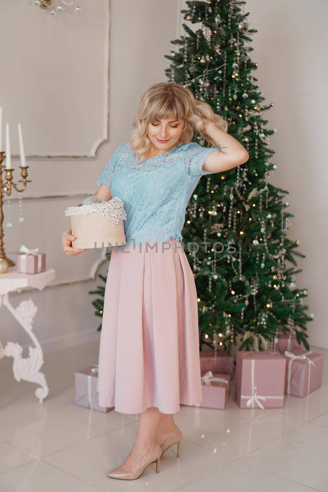 Young woman decorates Christmas tree with Christmas toys. Classic interior in white and gold