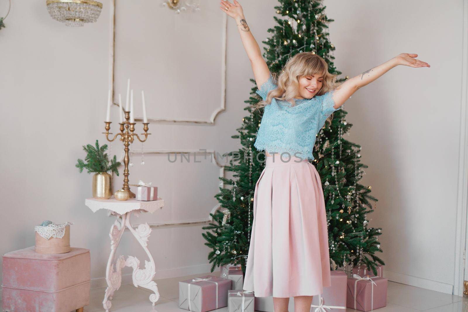 Beautiful woman near christmas tree smiling dancing in beautiful dress in decorated house, happy new year