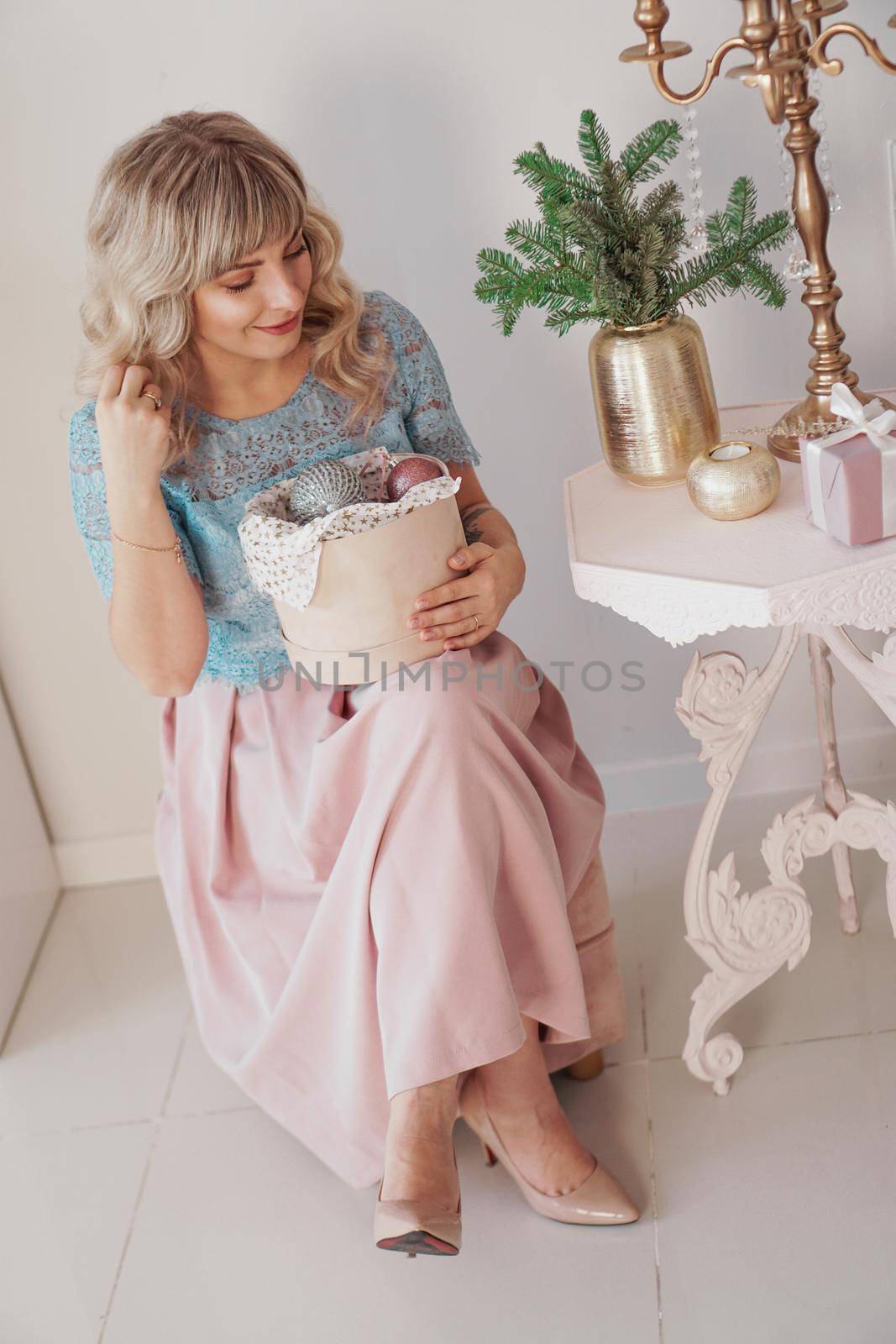 Young beautiful blonde woman holding a box of new year toys. Christmas and new year concept. Studio shot.