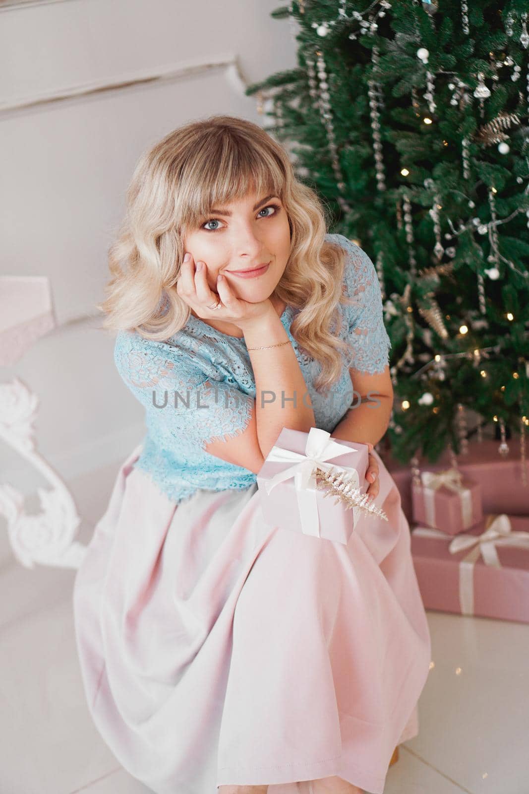 Lovely young woman with elegant style sitting indoor near decorated tree with pink Christmas presents