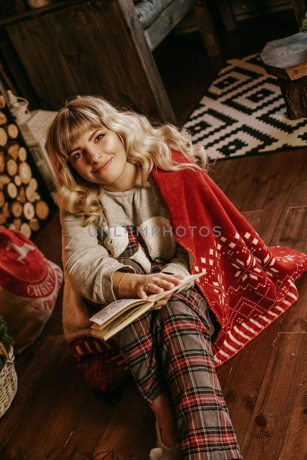 Happy young woman reading book in front of christmas interior with fireplace by natali_brill