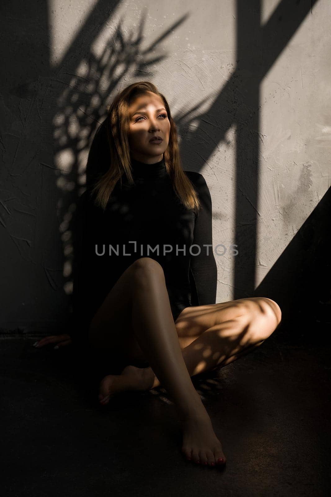 Fashion photo of sensual woman. She sits on the floor next to the window, a shadow on her