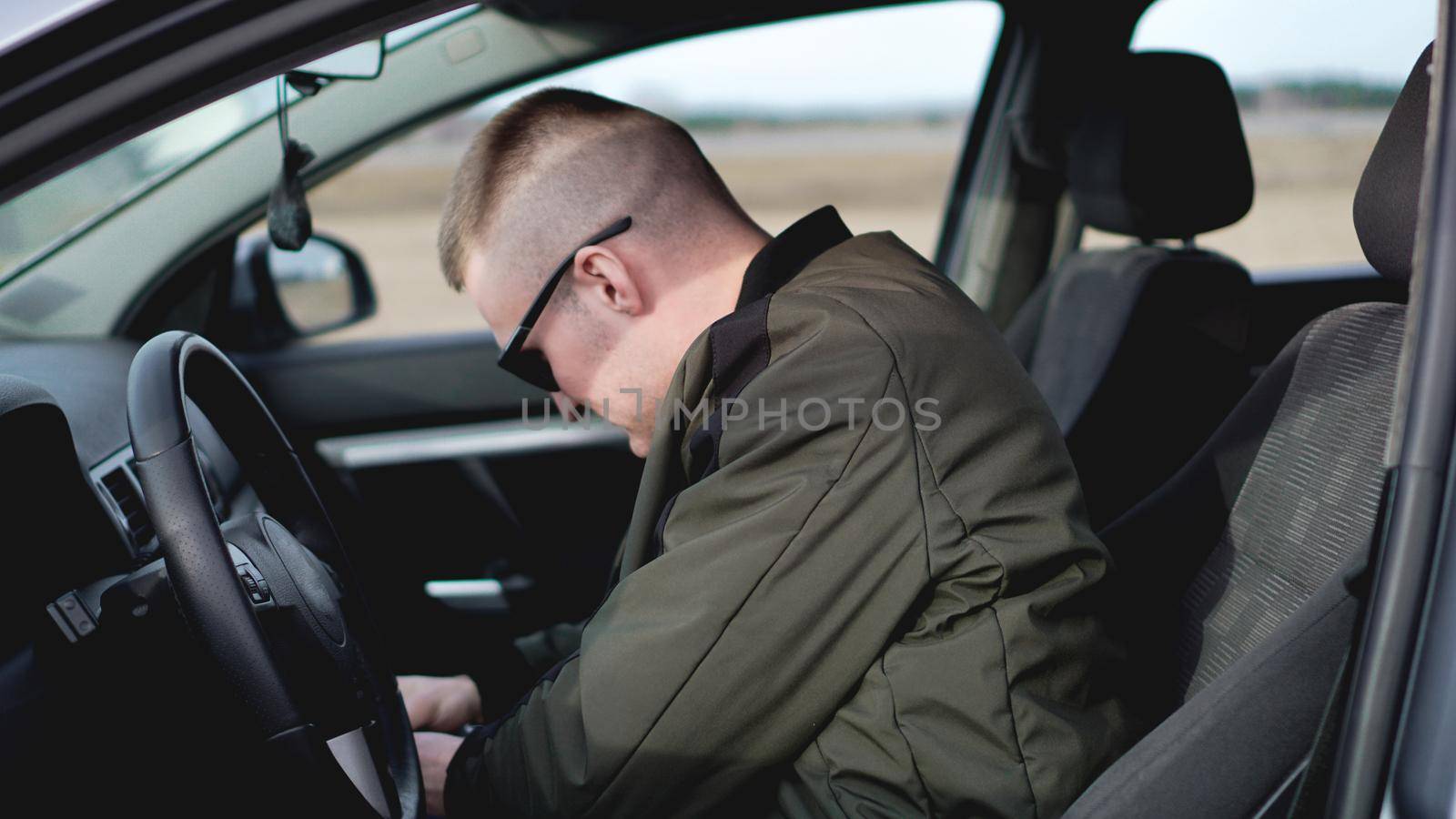 Side view of confident young stylish man in sunglasses looking for something in the passenger seat