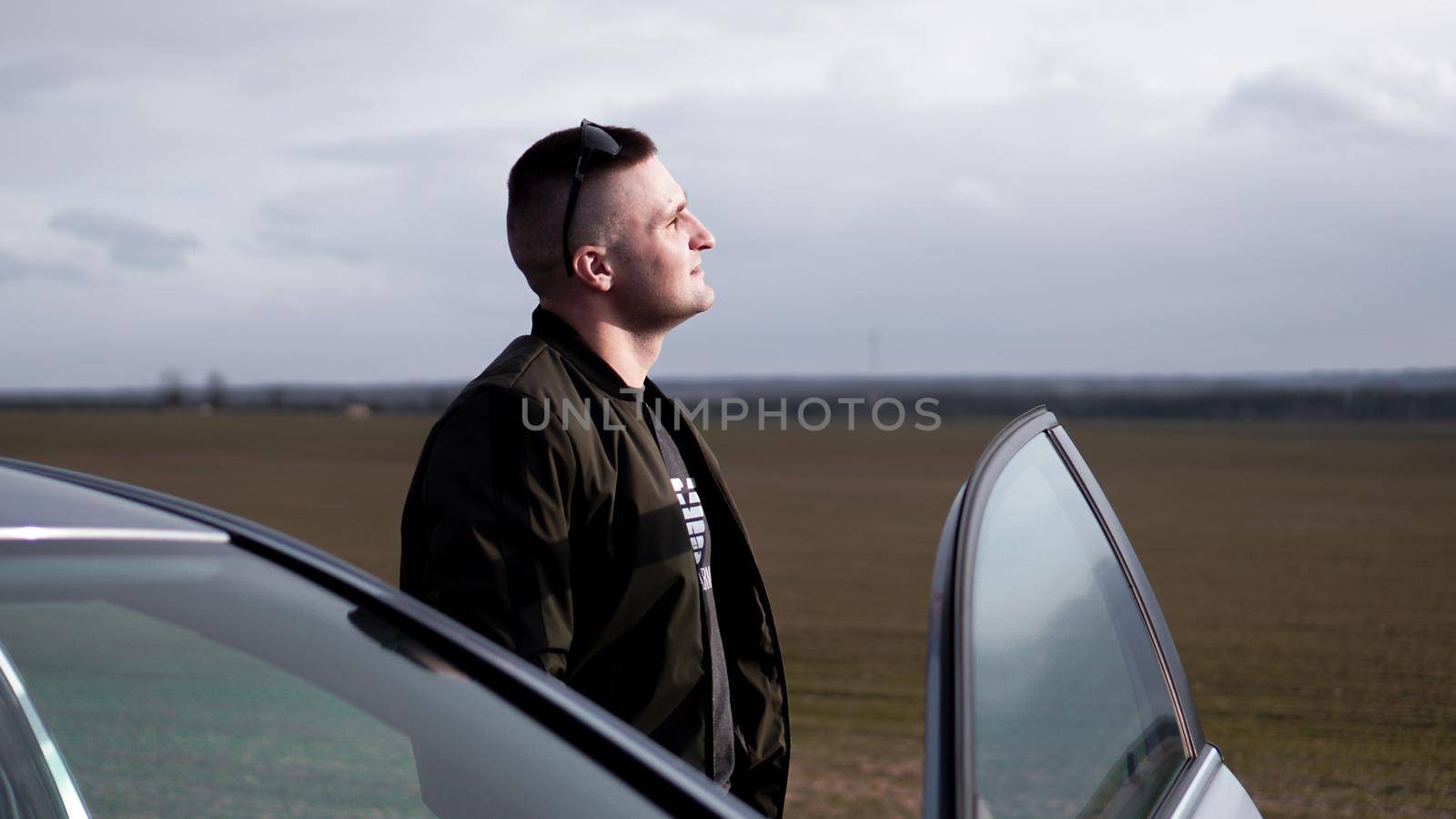 Handsome man standing near his new car on the background of the field