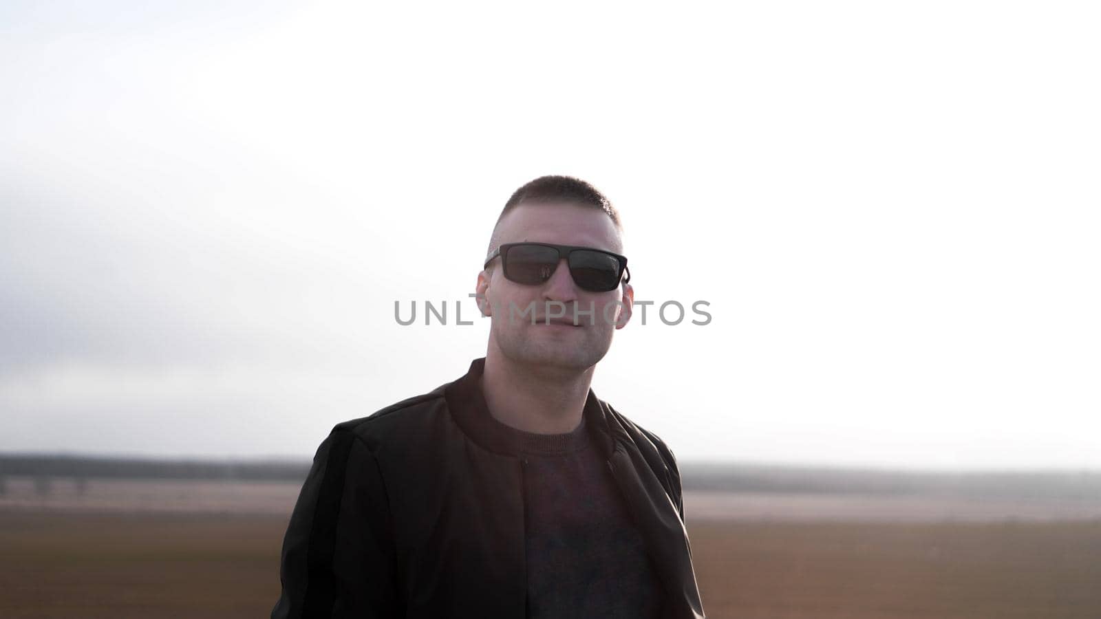 Handsome casual man wearing sunglasses standing outside in a grass field by natali_brill