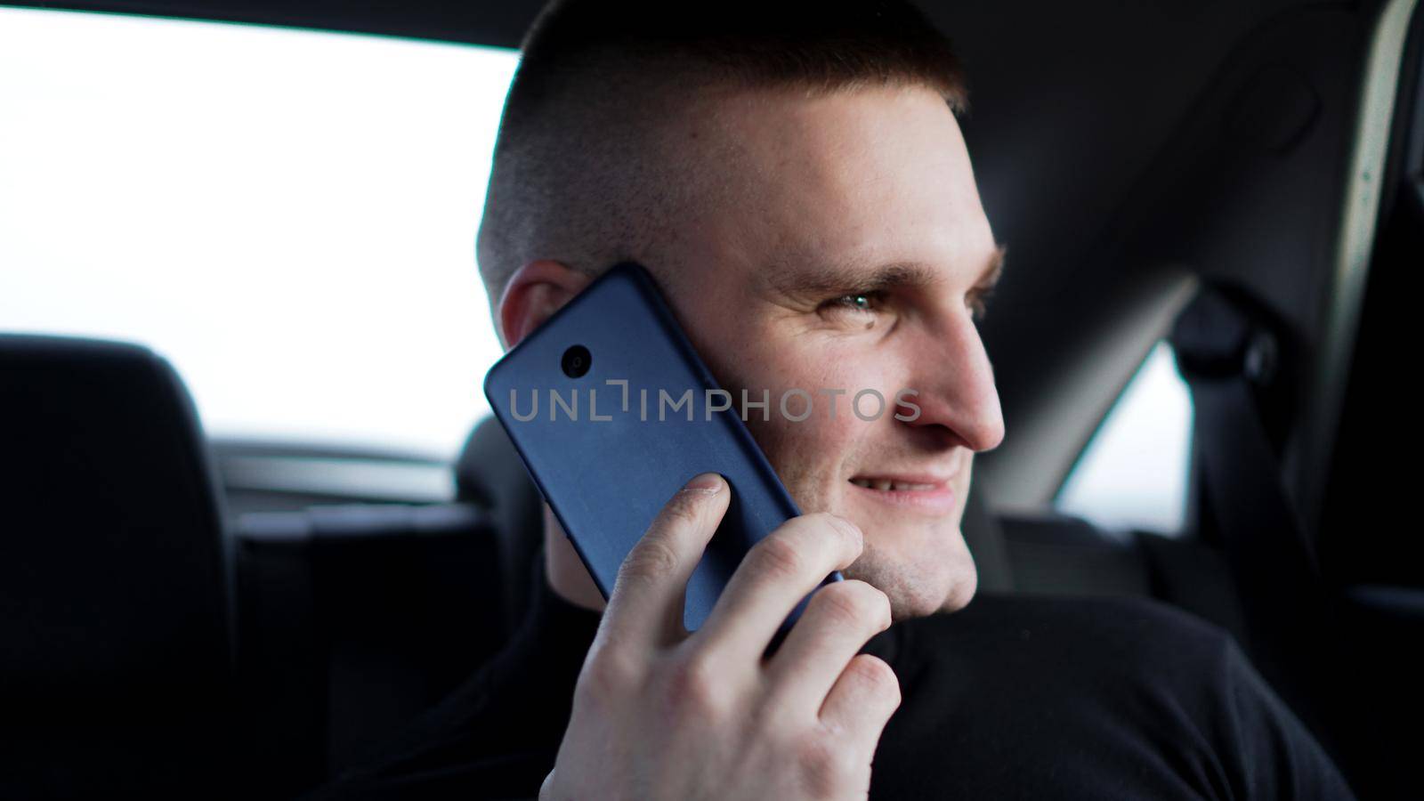 Young confident businessman talking on mobile phone while sitting on back seat of a car