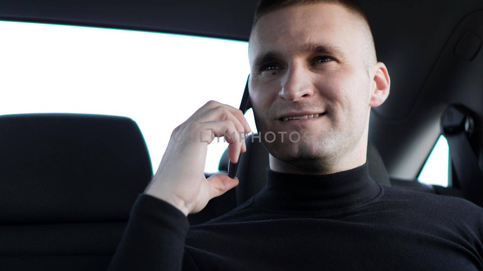 Young businessman talking on mobile phone while sitting on back seat of a car by natali_brill