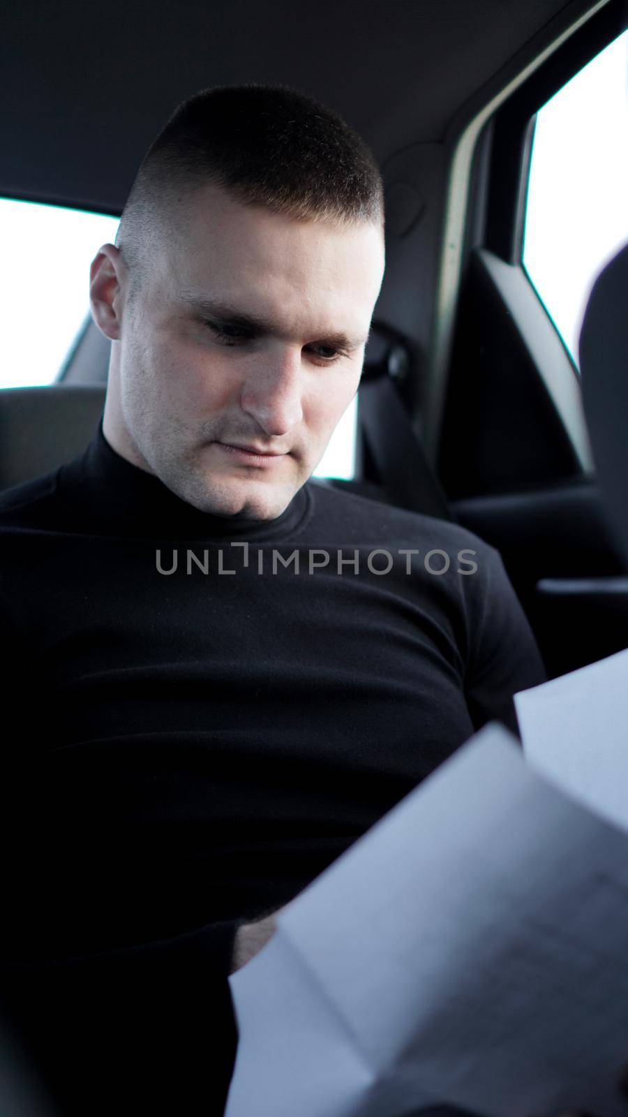 Young businessman looking through documents while sitting at the back of a car