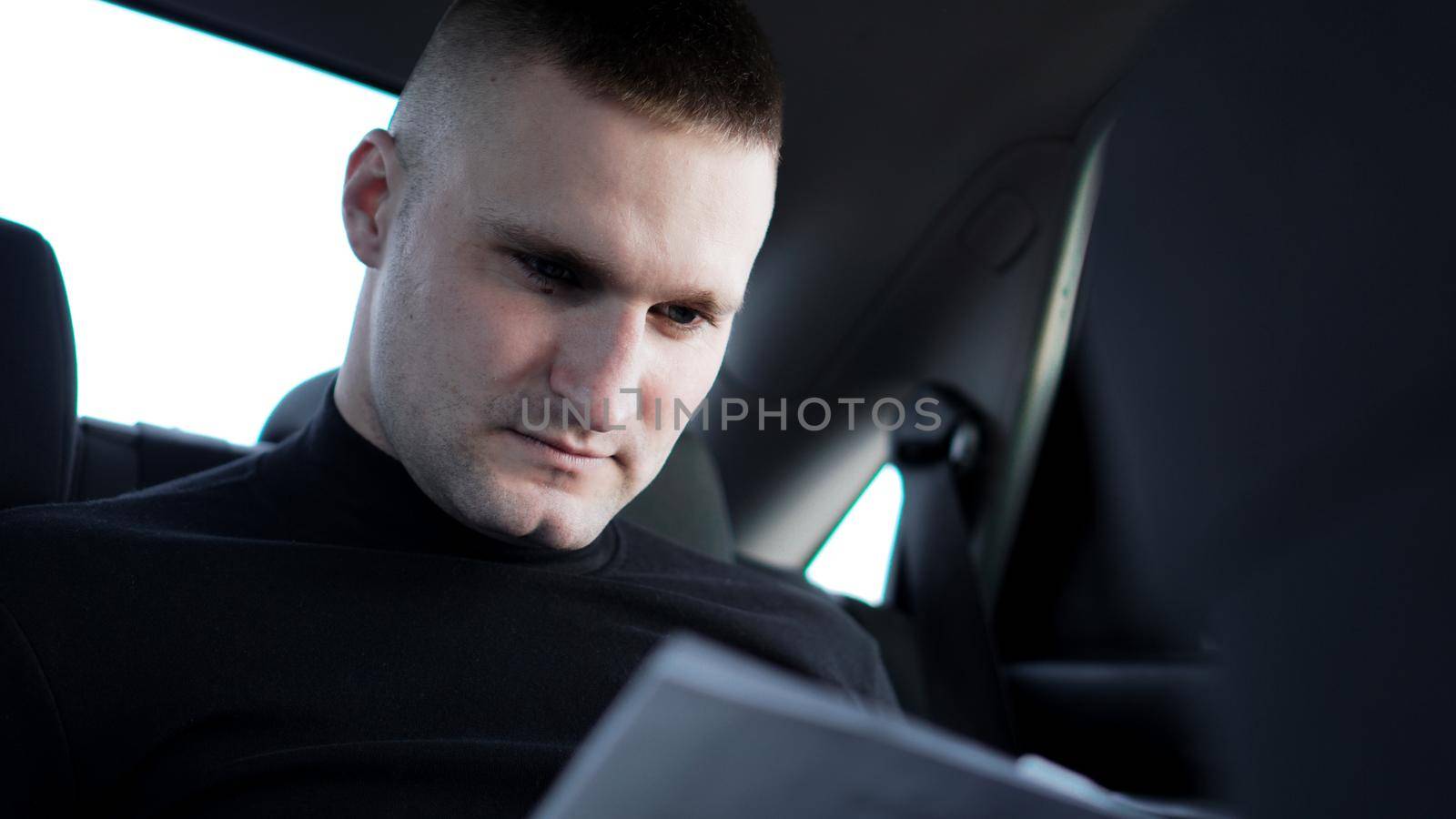 Young businessman looking through documents while sitting at the back of a car