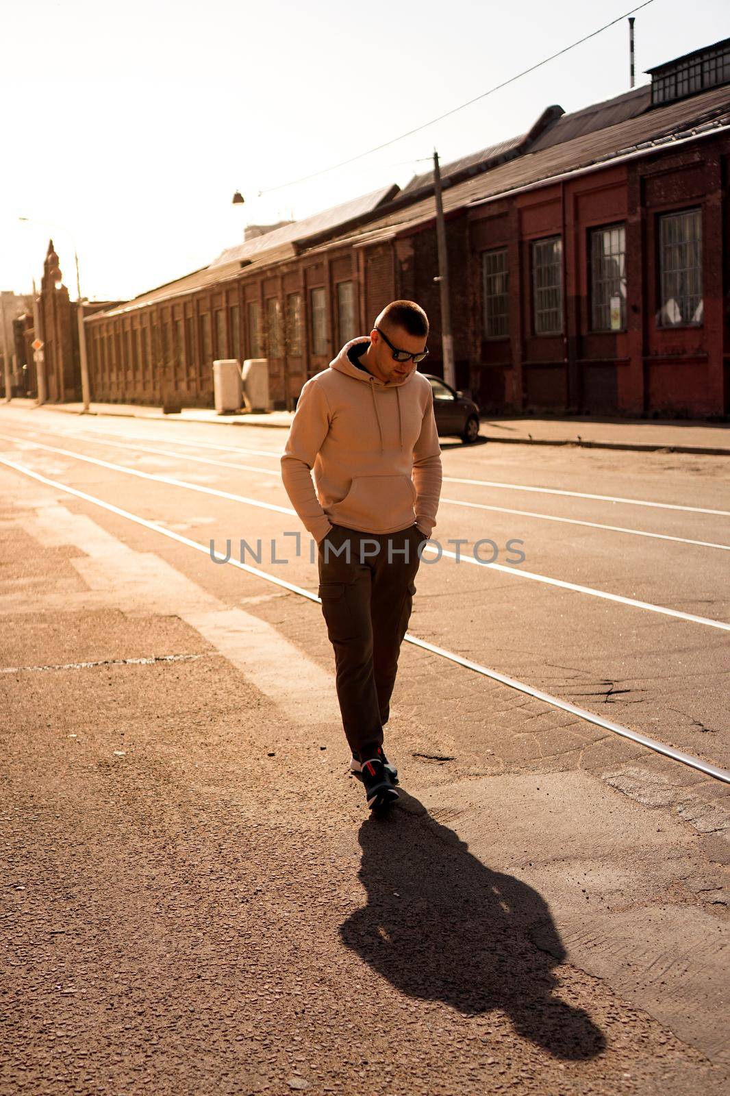 Hipster walking in the street with red brick wall building in summer day. Young man in full growth. Lifestyle photo