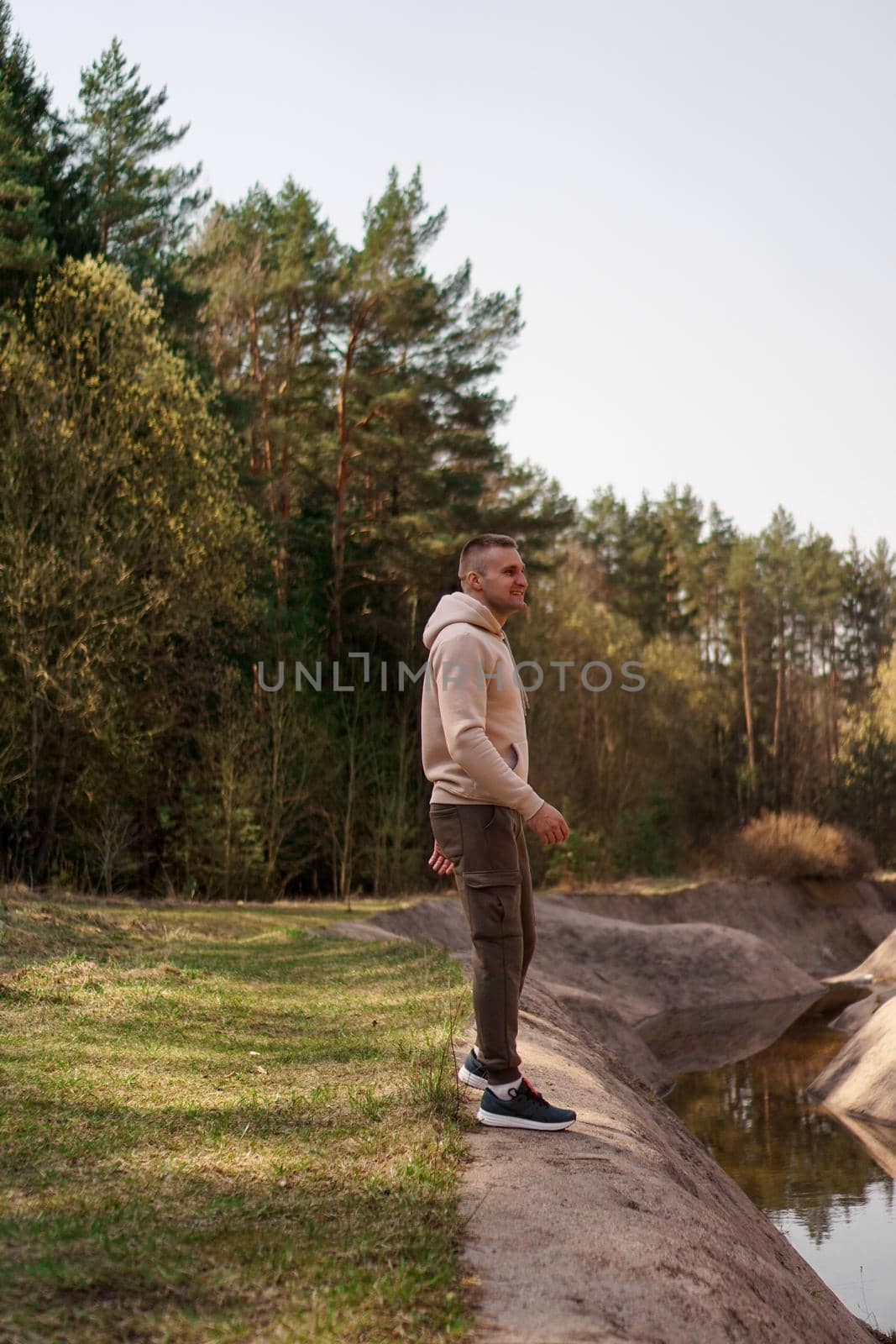 A young man in a comfortable suit walks through the forest by the river. by natali_brill