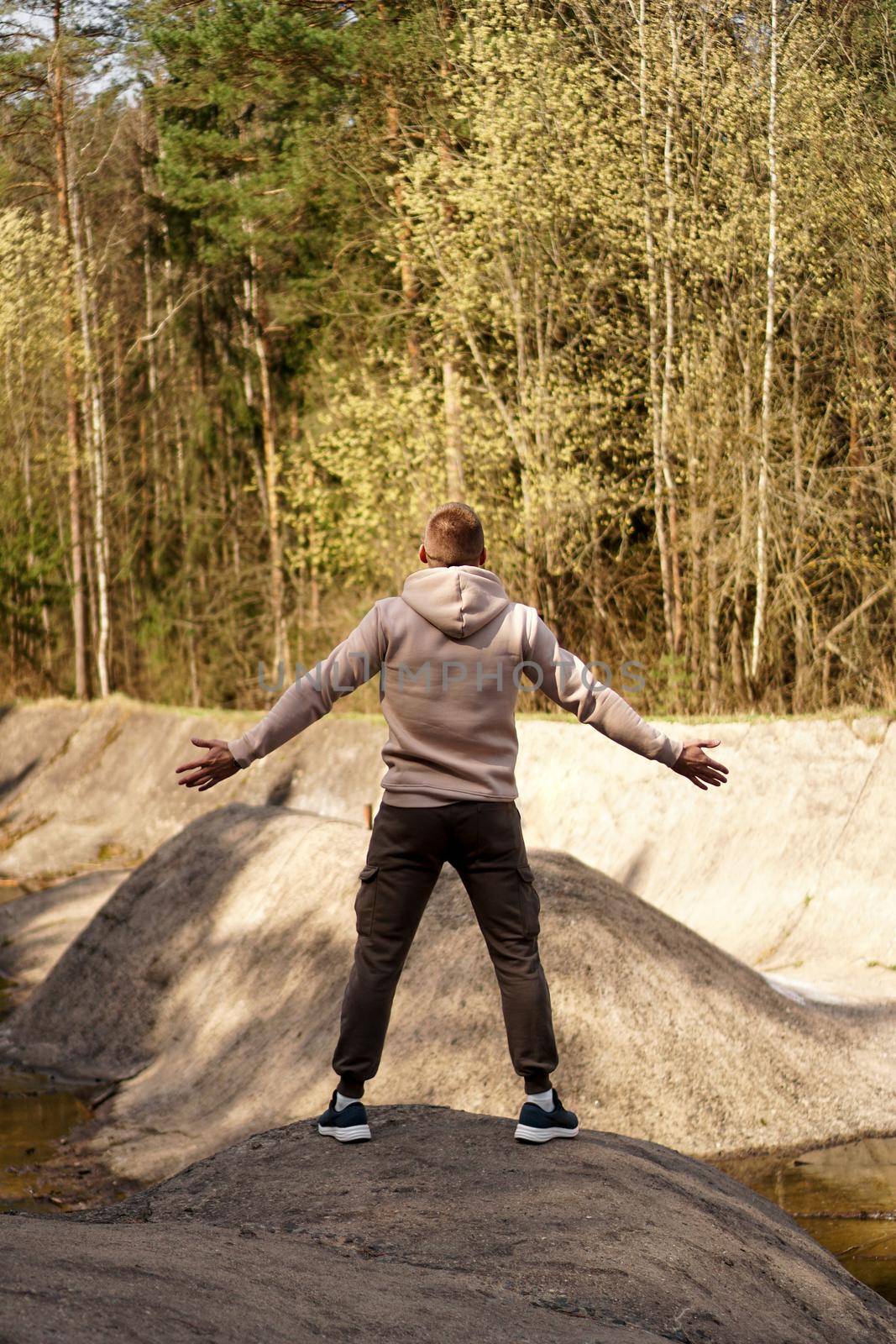 A young man stands on a small mountain in the area of a mountain river and spread his arms to the sides. The concept of success and conquering the mountains.