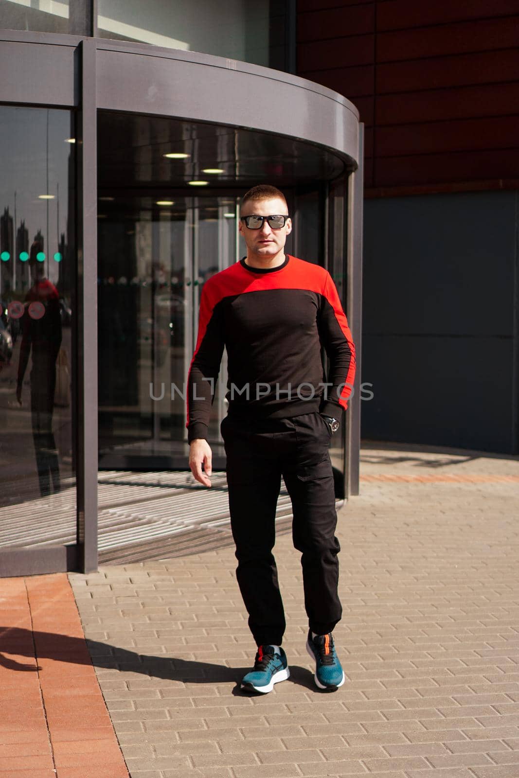A young athletic man in a tracksuit walks out of the revolving doors by natali_brill