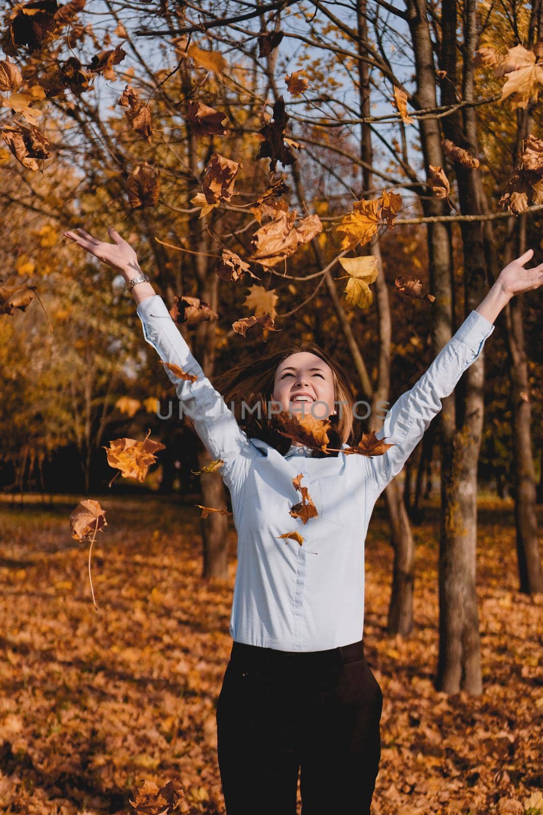Woman throwing yellow leaves in the air - autumn park