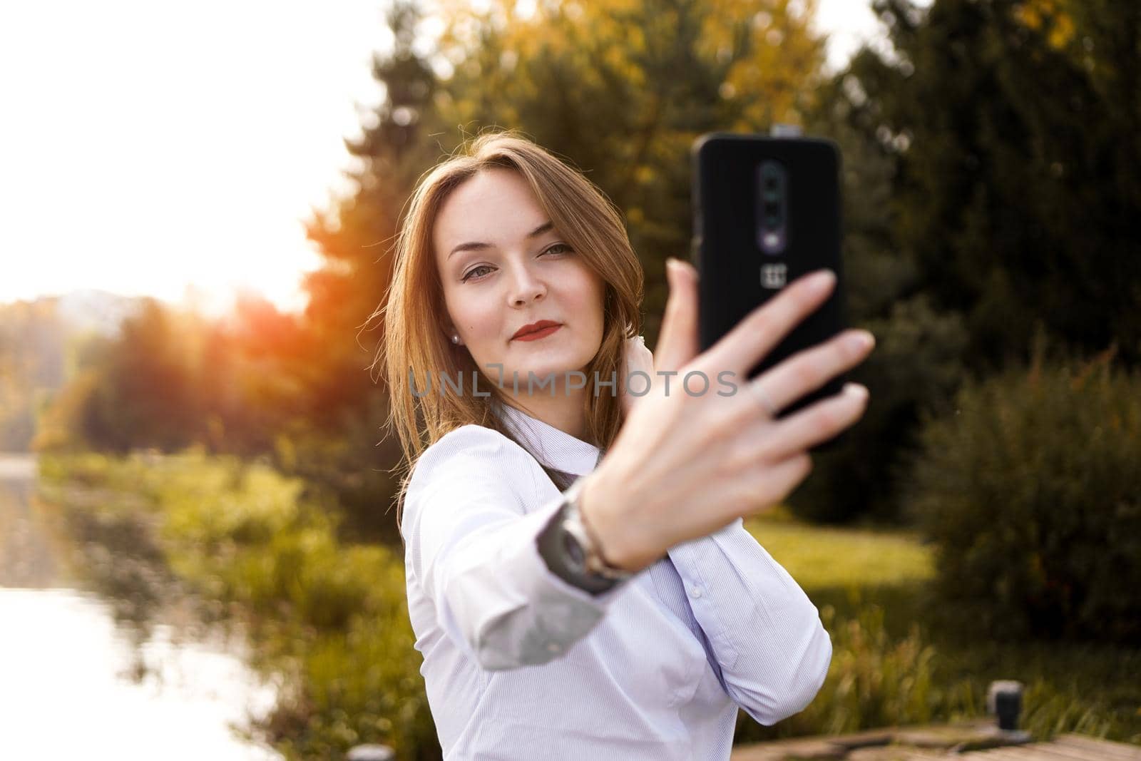 Portrait of cheerful young woman making selfie in park