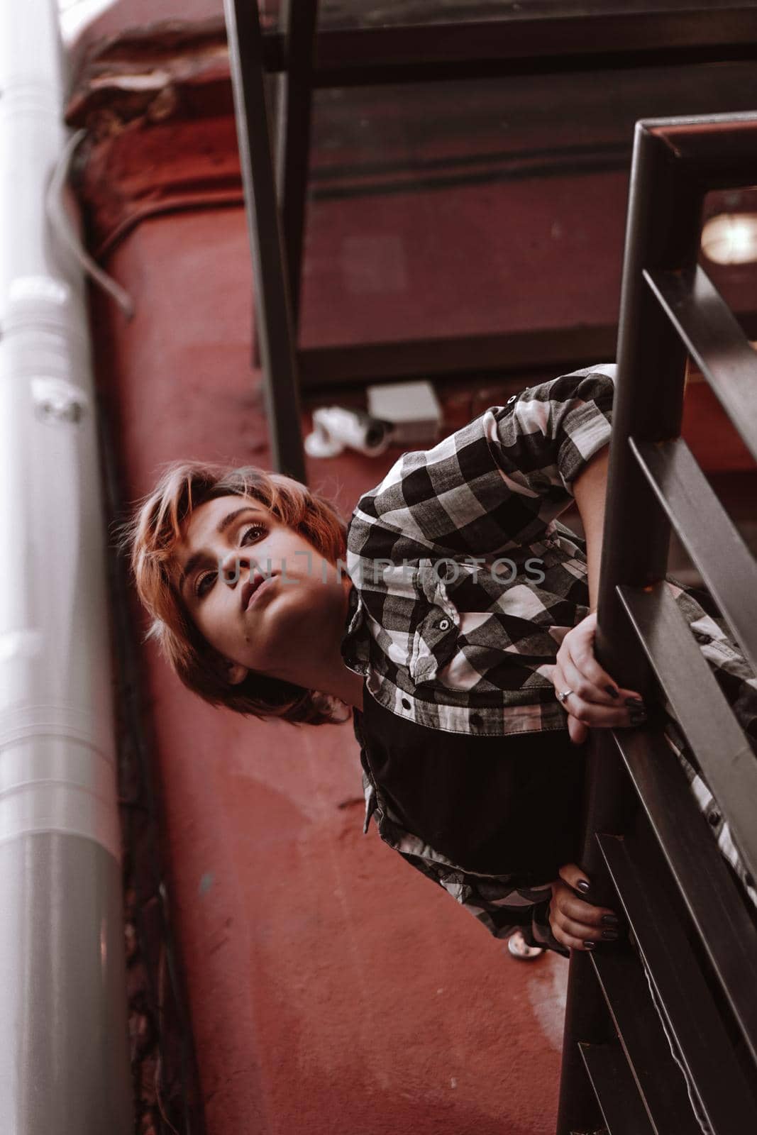 Beautiful young woman with short red hair in plaid shirt in the old city with red walls