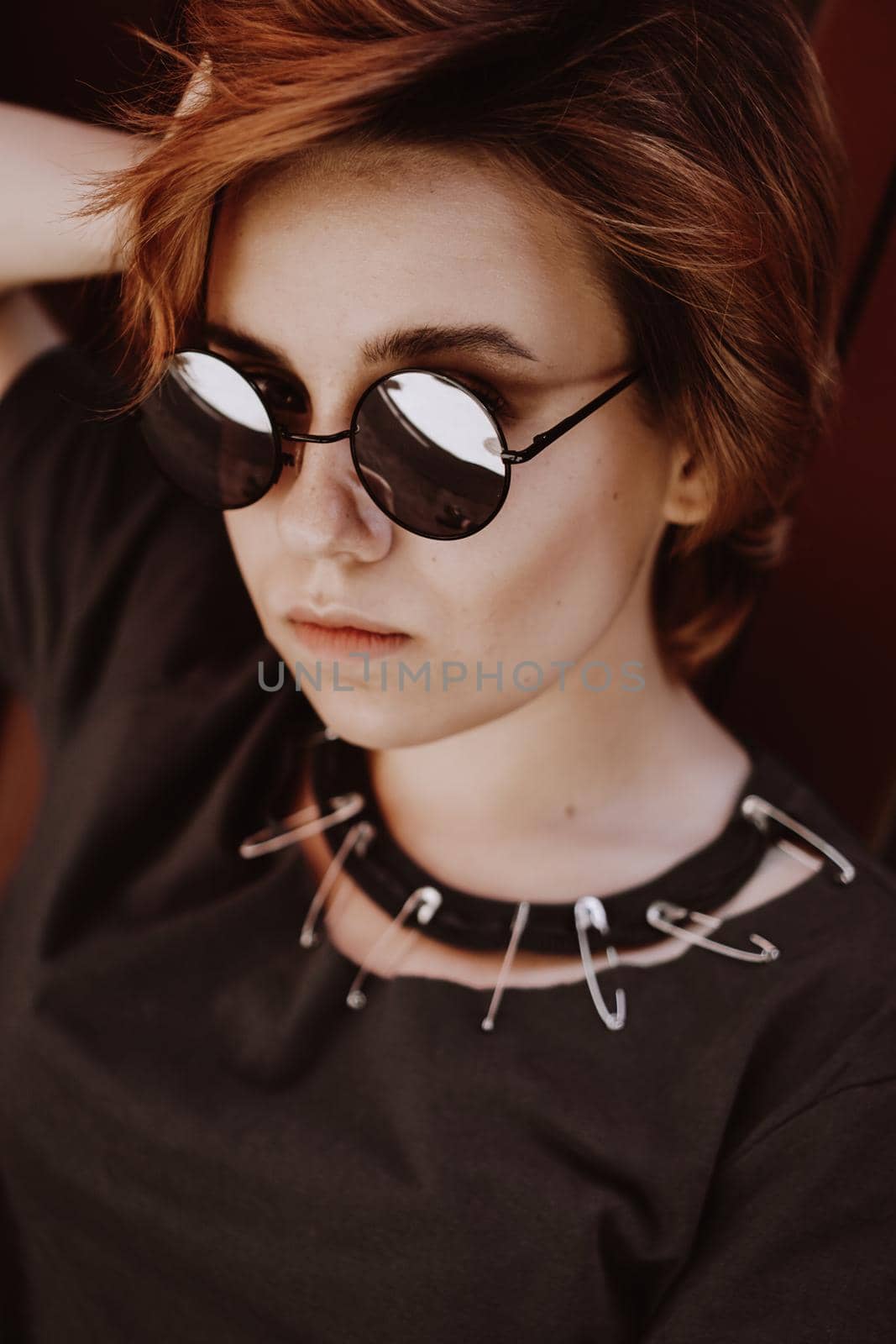 Portrait of attractive cheeky woman with short red hair in sunglasses at back yard in the old city with red walls