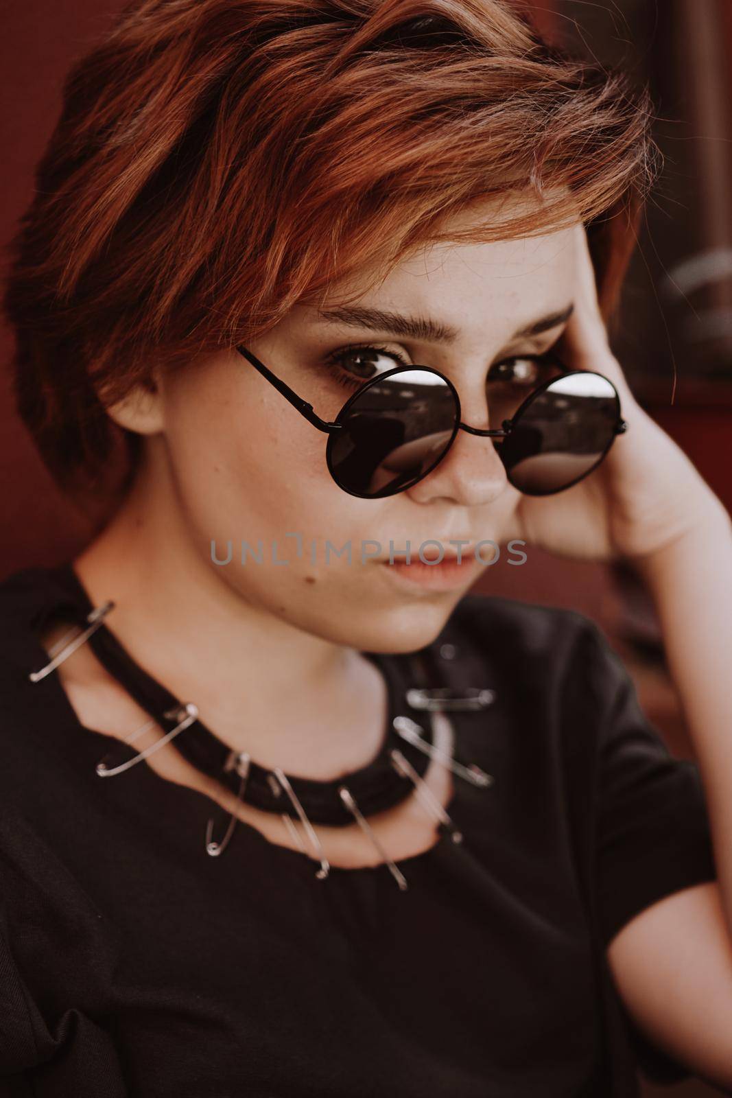 Portrait of attractive cheeky woman with short red hair in sunglasses at back yard in the old city with red walls