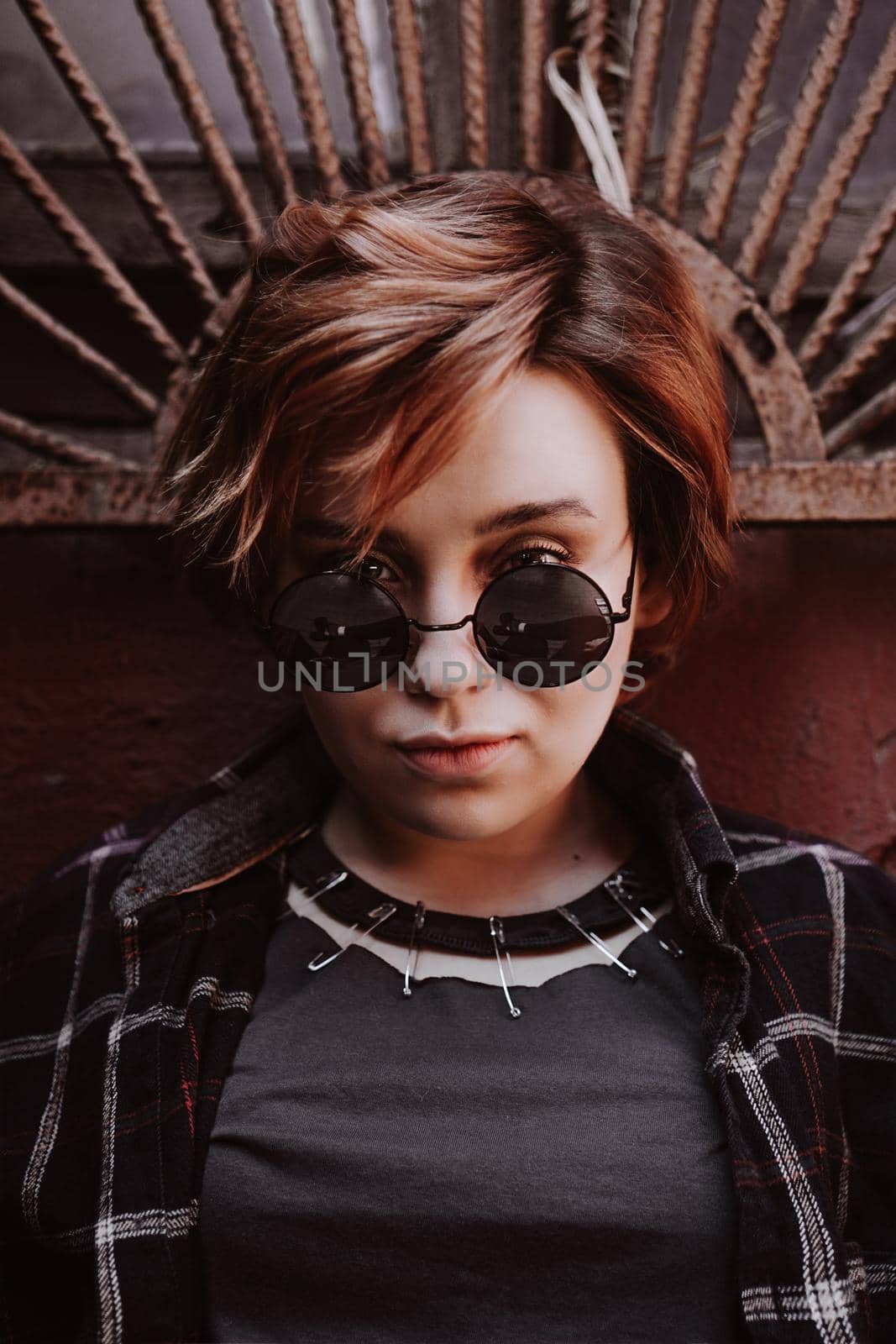 Portrait of attractive cheeky woman with short red hair in sunglasses at back yard in the old city with red walls