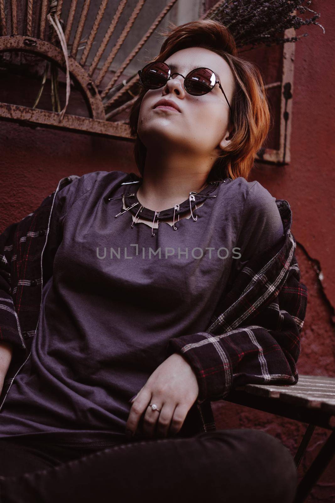 Portrait of attractive cheeky woman with short red hair in sunglasses at back yard in the old city with red walls