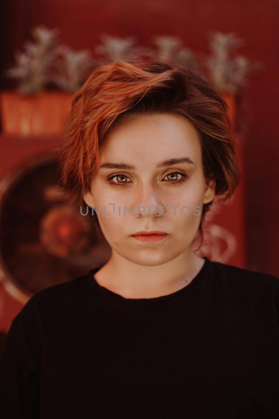 Portrait of attractive cheeky woman with short red hair at back yard in the old city with red walls