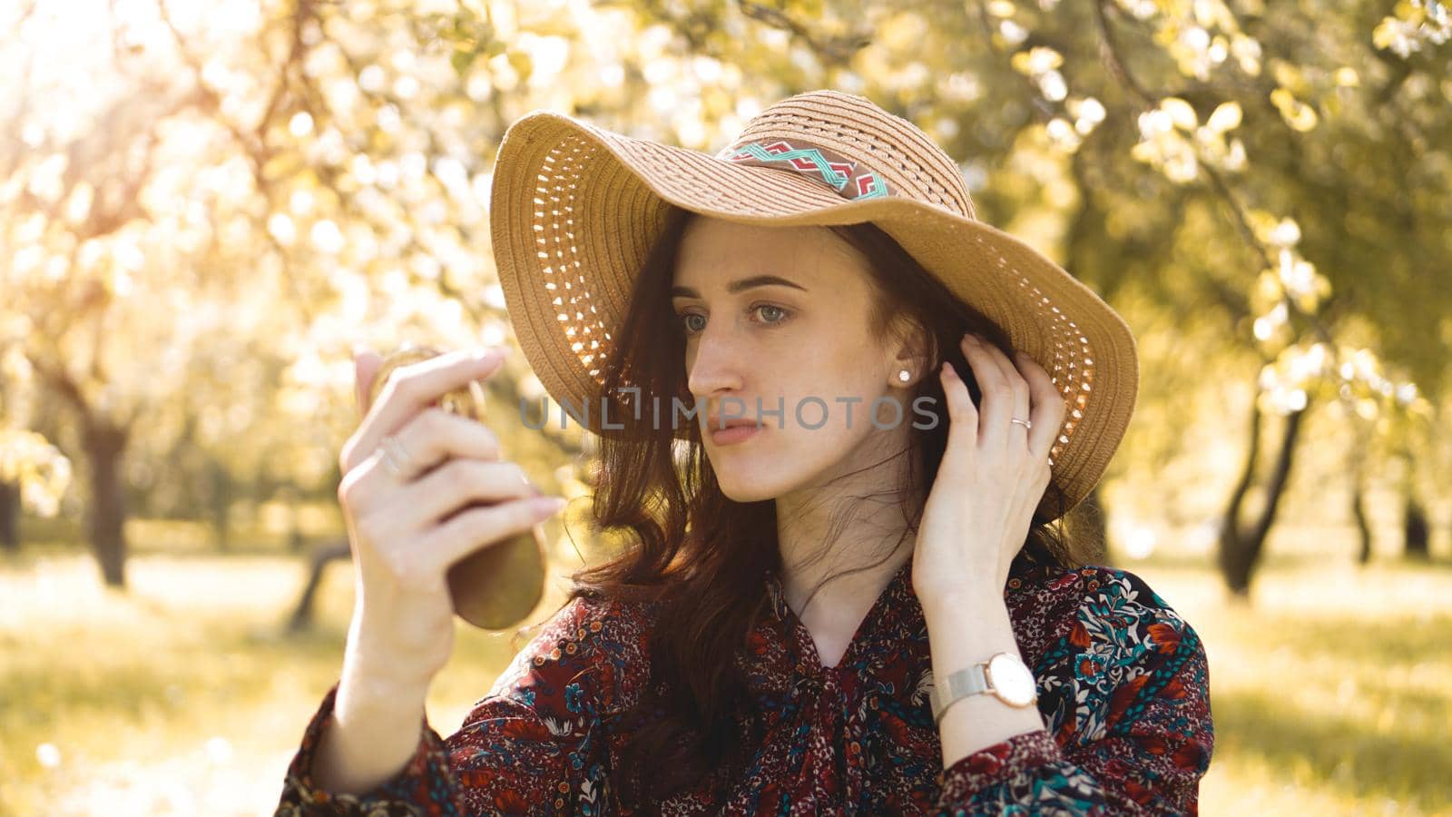 Close up of a pretty young woman in hat fixing her make up while looking at the mirror outdoors