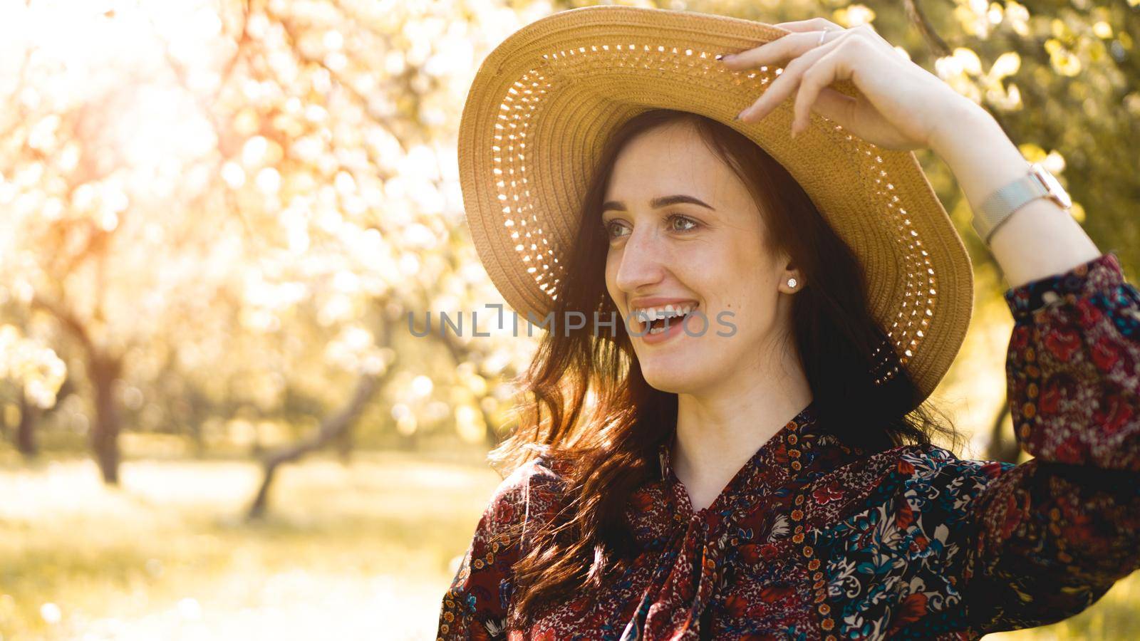 Summer portrait, beautiful young woman wearing straw hat at sunset time on the garden