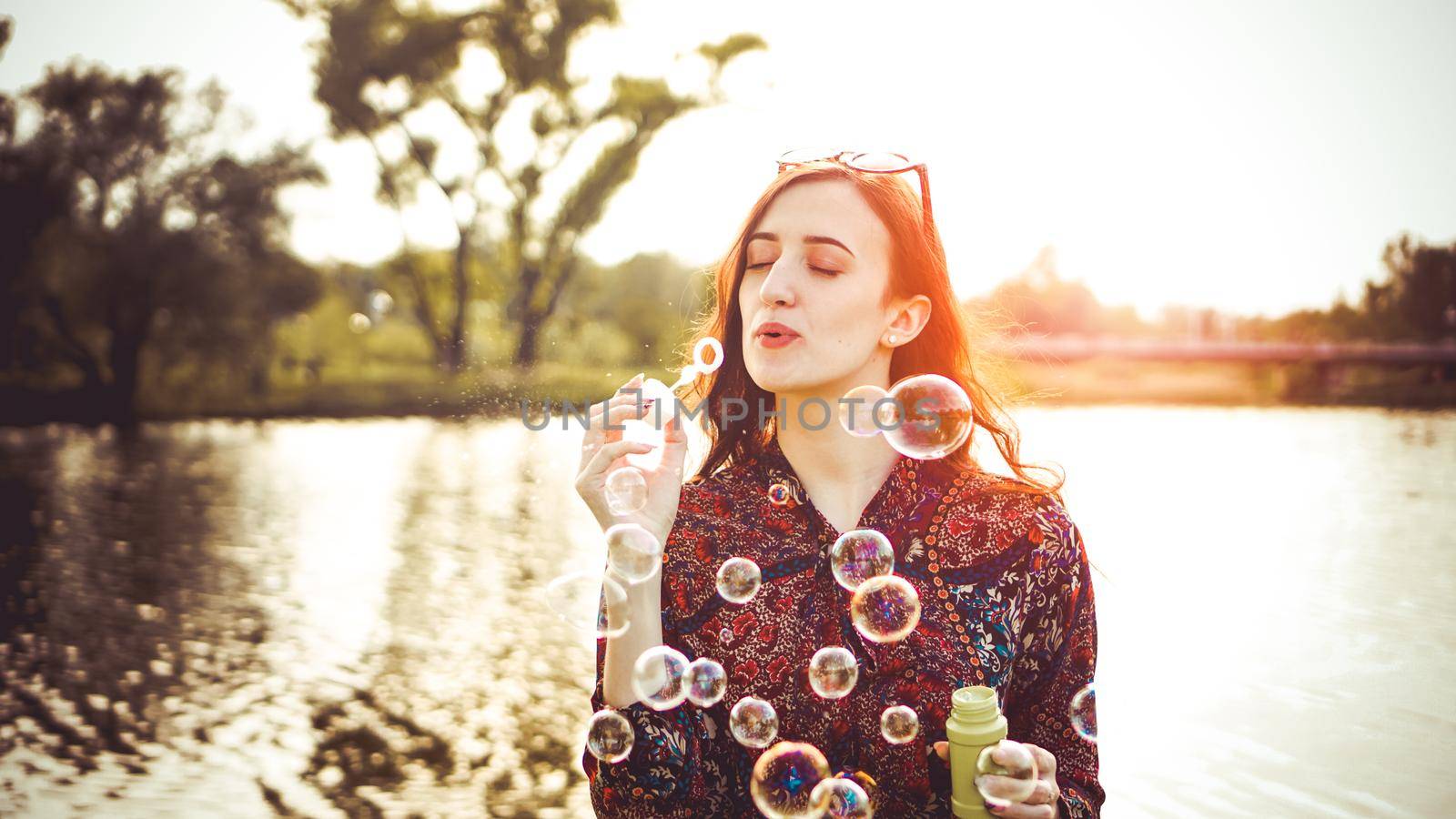 Romantic portrait of young woman with soap balloons. Sunny Valley and river on a summer day
