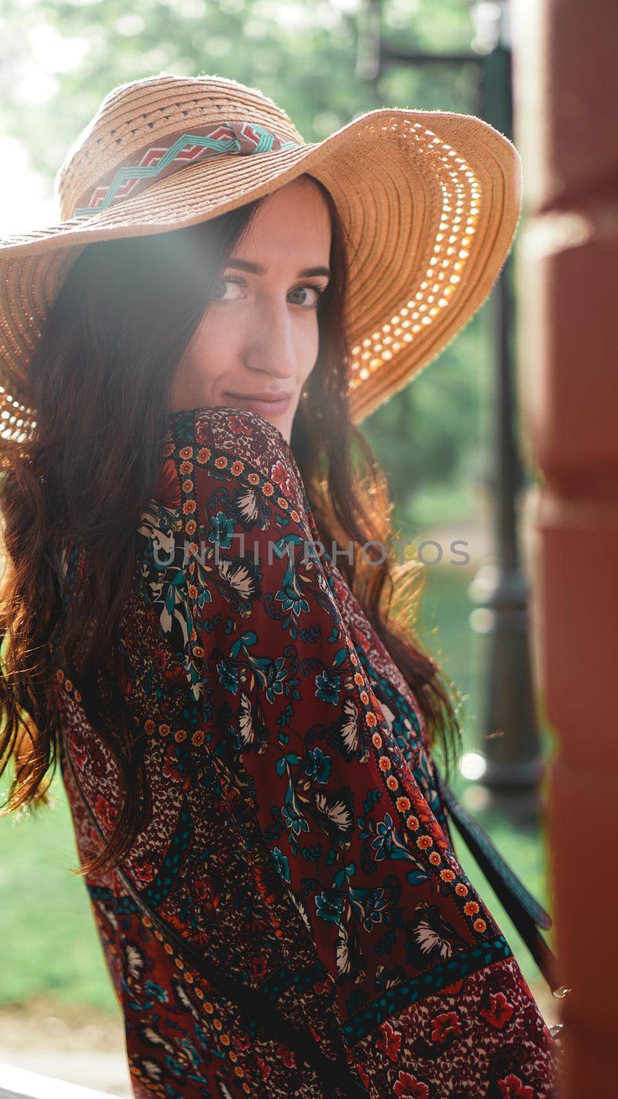 Portrait of pretty woman wearing dress and straw hat in sunny warm weather day. Walking at summer park.