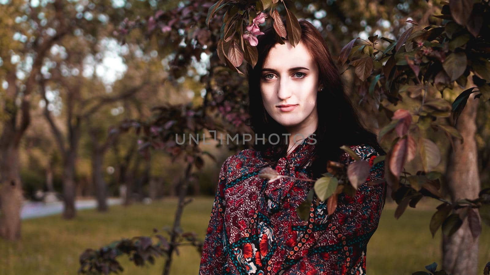 Beautiful young woman by branches with burgundy and green leaves. Romantic fashion look. Dreamy girl