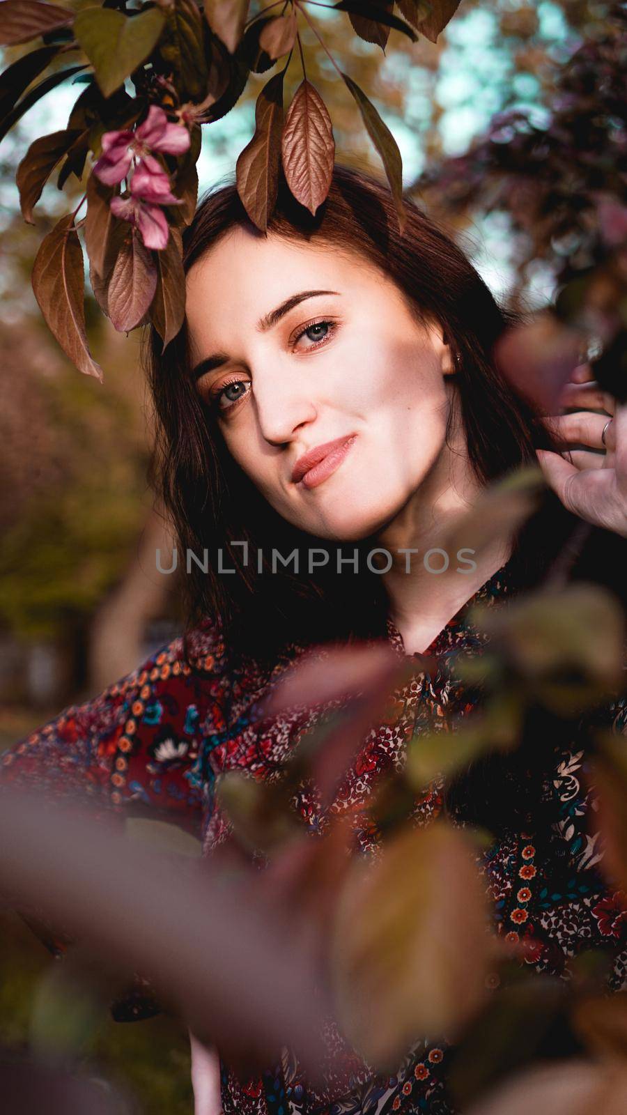 Beautiful young woman by branches with burgundy and green leaves. Romantic fashion look. Dreamy girl