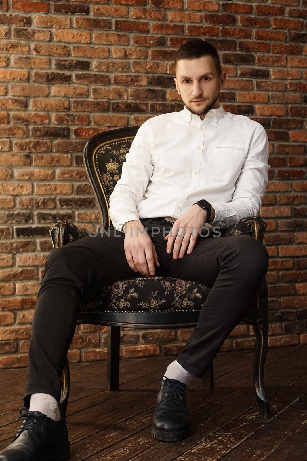 Portrait handsome fashionable man in a white shirt sits on a chair in a photo studio loft. Young businessman is thinking about future