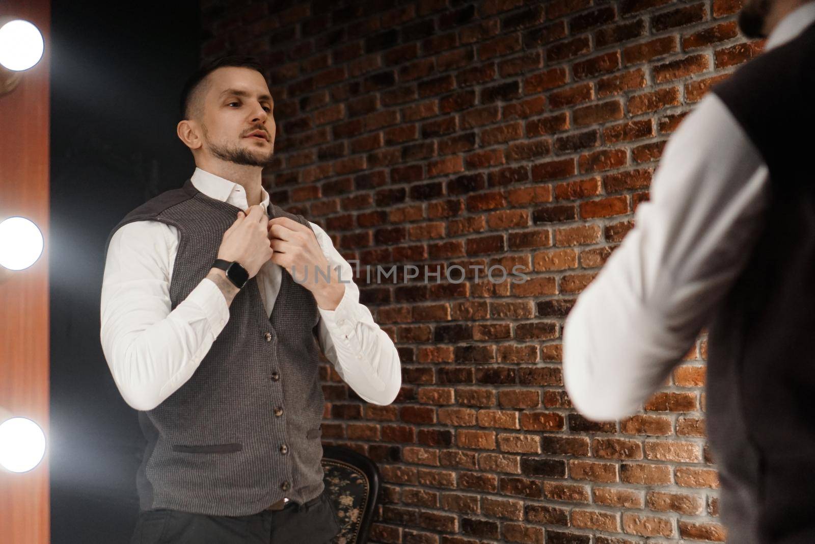 Stylish confident young man looking at himself in mirror by natali_brill