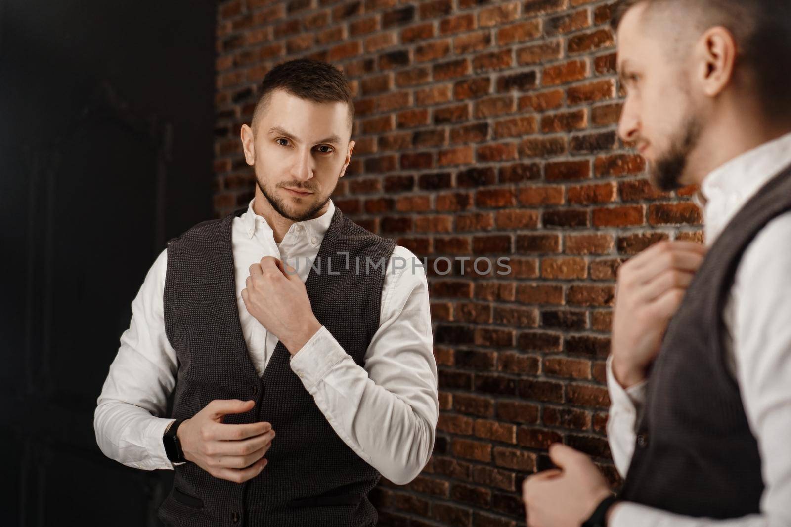 Stylish confident young man looking at himself in mirror. Fitting a suit in a store or sewing studio - loft interior