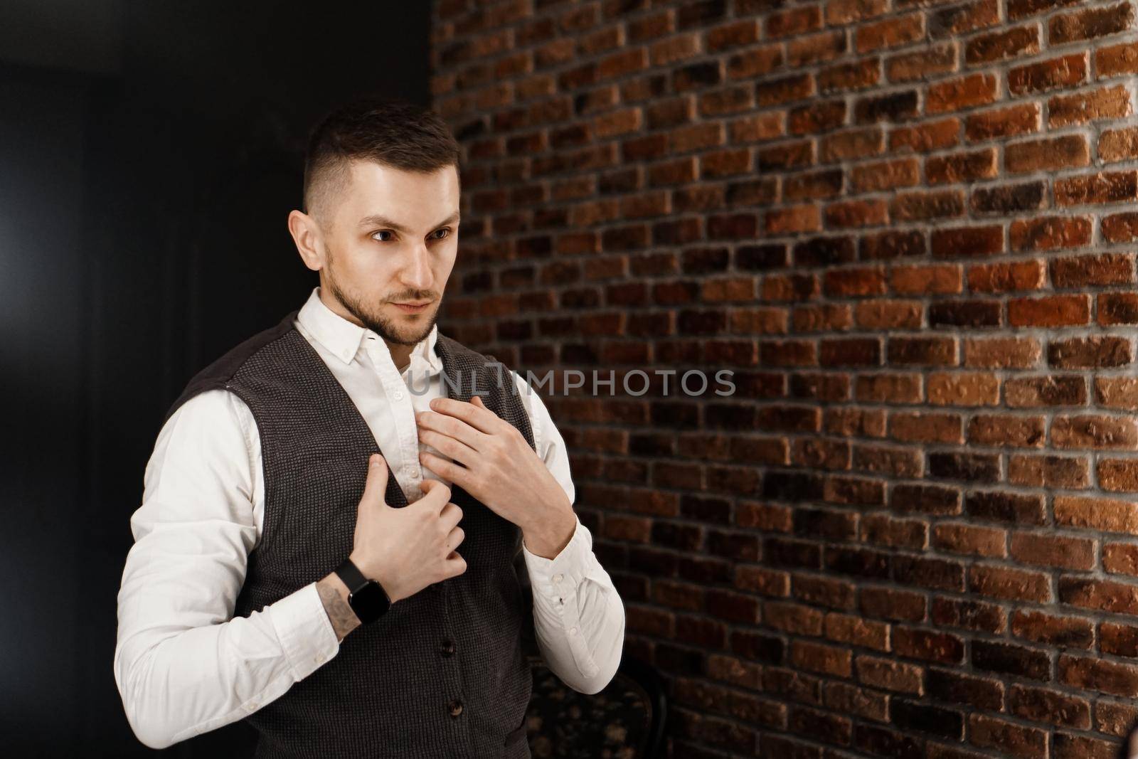 Stylish confident young man looking at himself in mirror. Fitting a suit in a store or sewing studio - loft interior