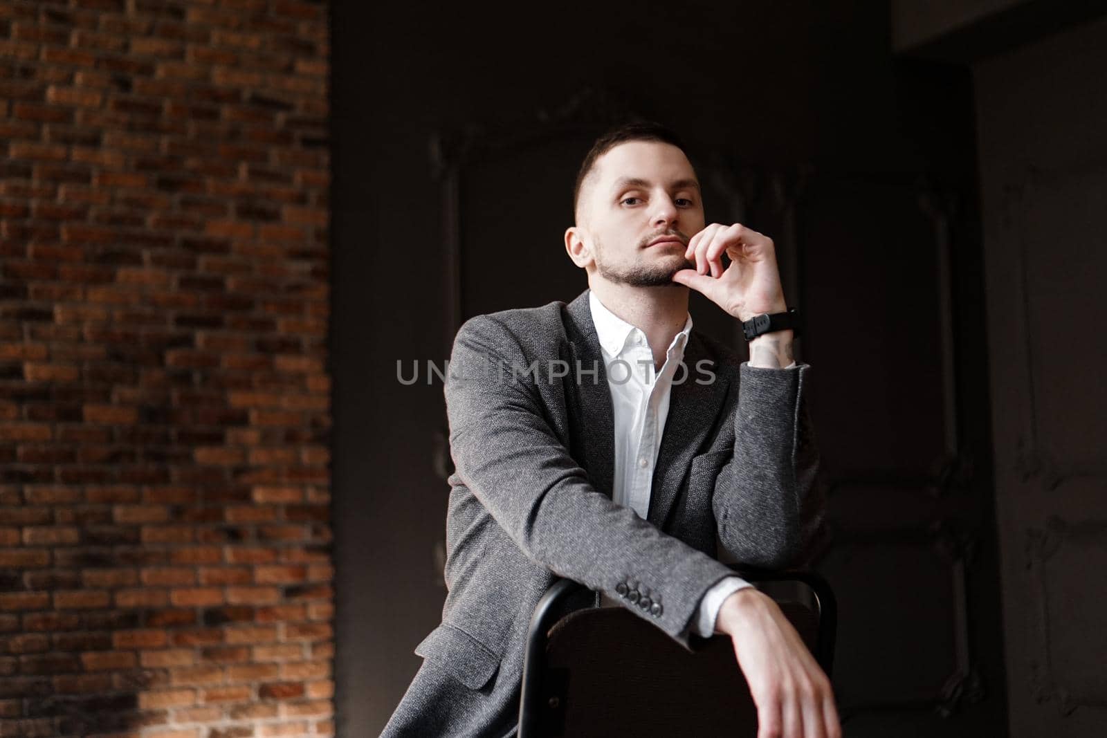 Portrait handsome fashionable man in a white shirt sits on a chair in a studio by natali_brill