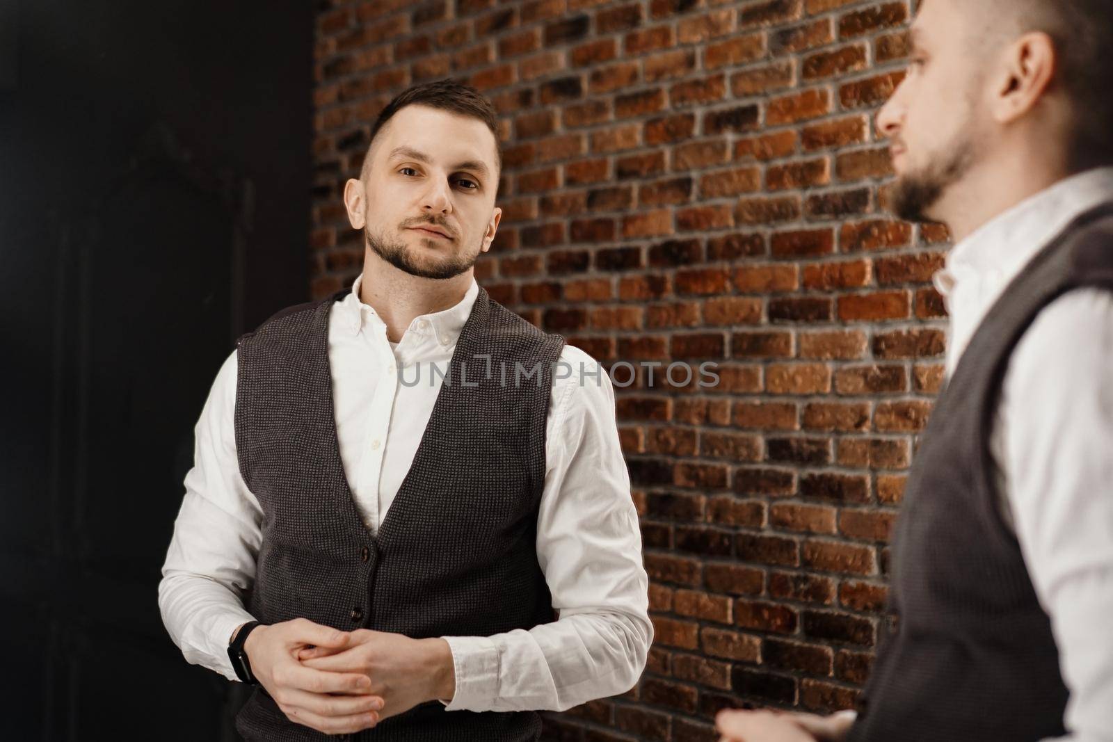 Stylish confident young man looking at himself in mirror. Fitting a suit in a store or sewing studio - loft interior