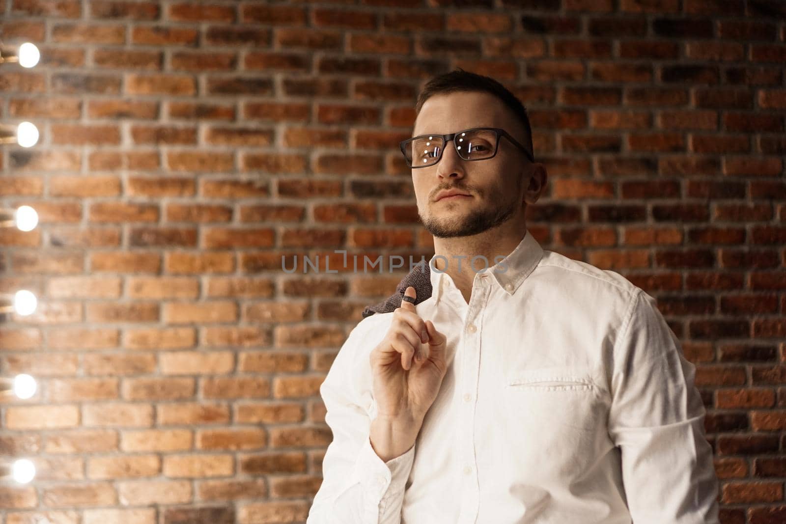 Handsome man in white shirt with glasses standing near red brick wall
