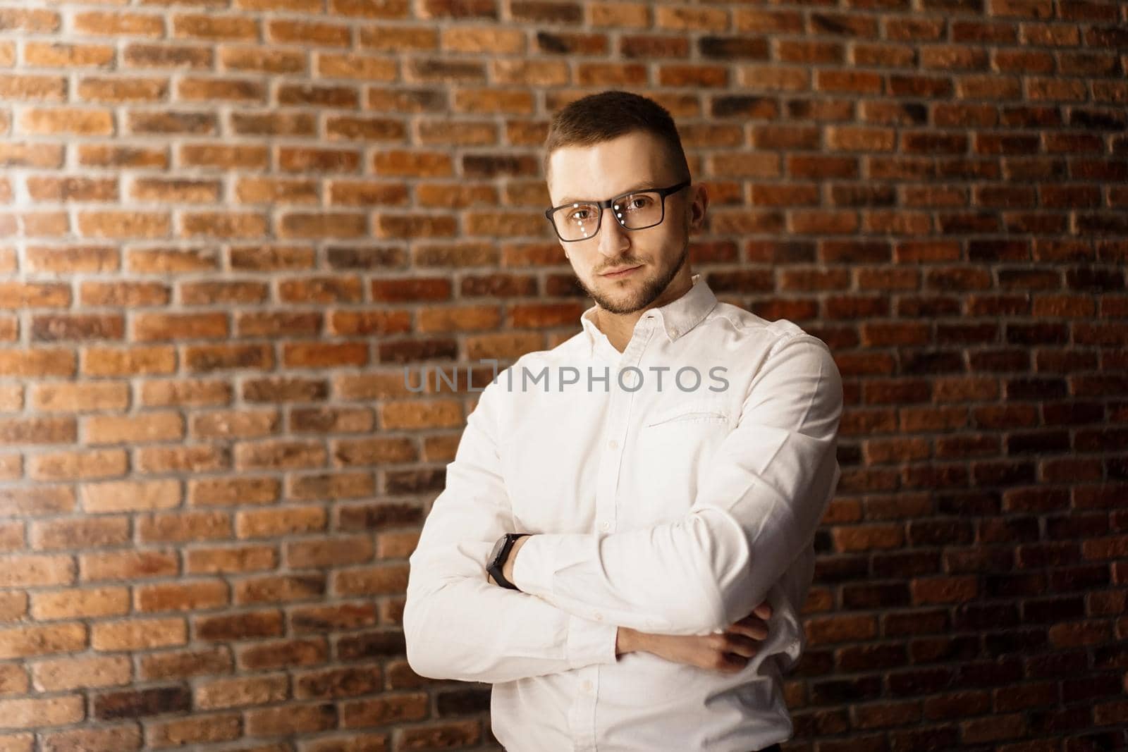 Handsome man in white shirt with glasses standing near red brick wall