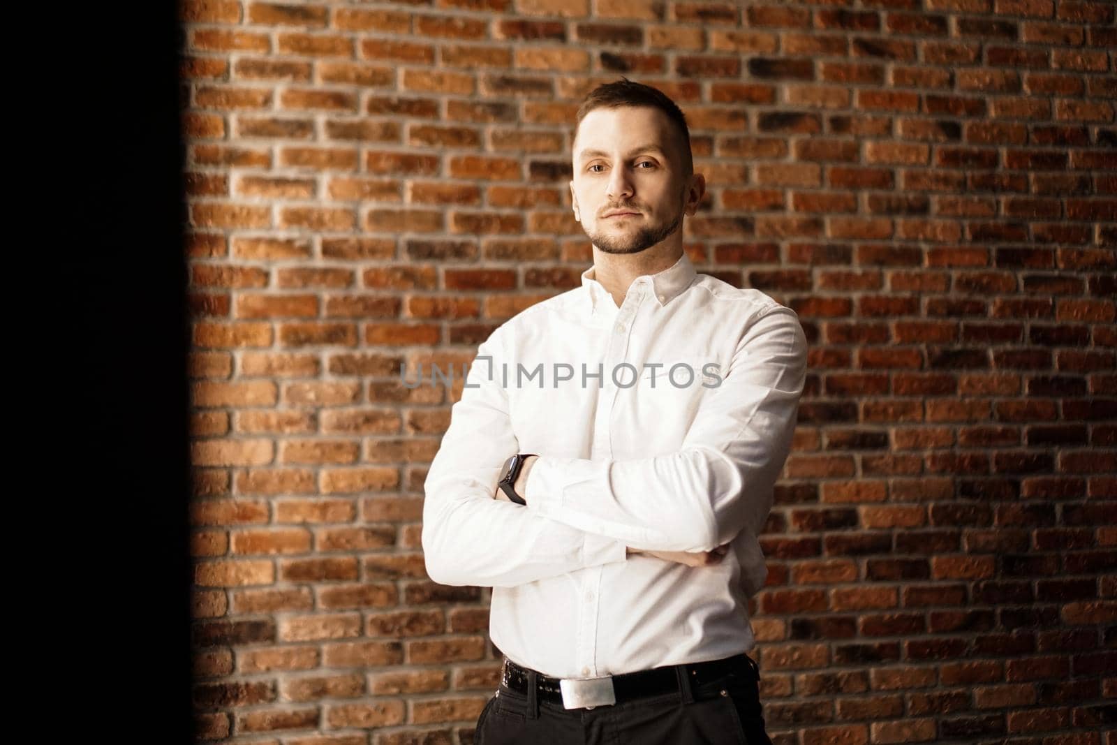Handsome man with arms crossed in white shirt standing near red brick wall