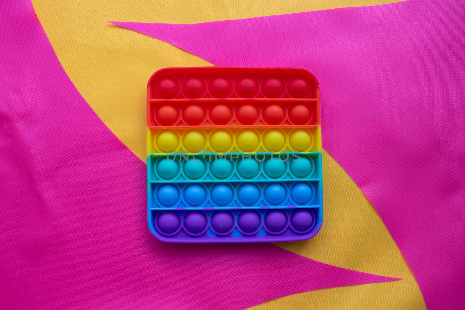 Pop it. A toy on a pink and yellow fabric background. Blue and Orange Funny Interactive Anti-Stress Silicone Toys.