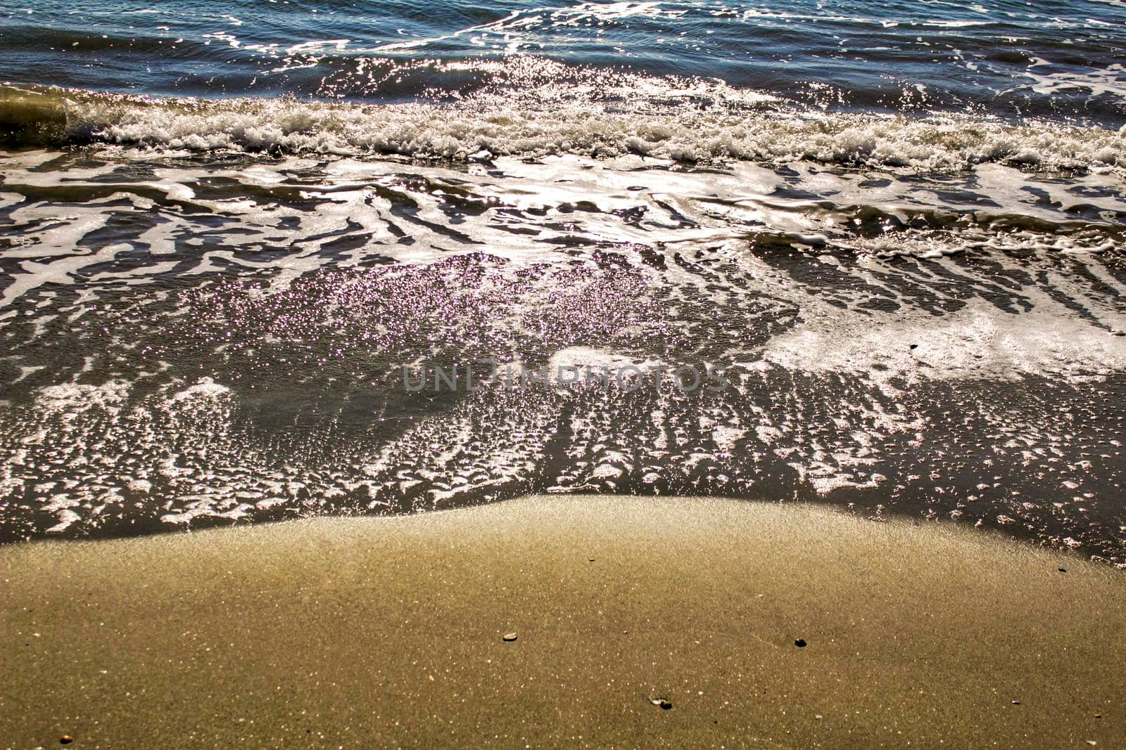 Waves, light and sand texture on the beach in the morning
