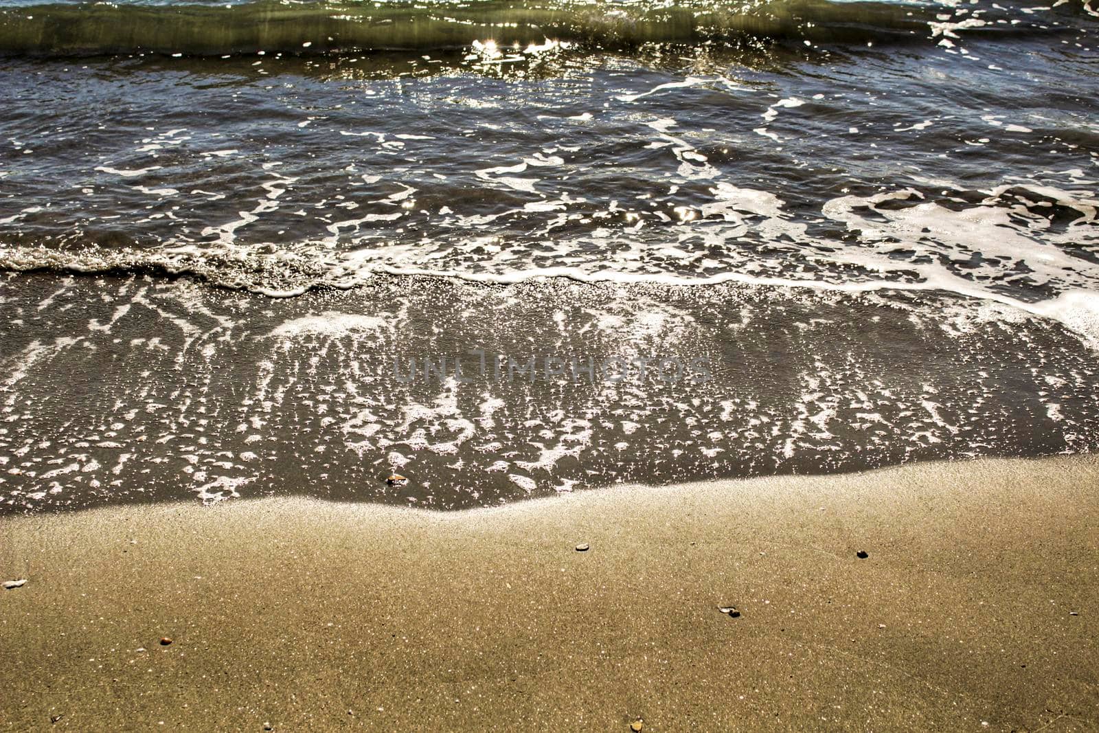 Waves, light and sand texture on the beach in the morning