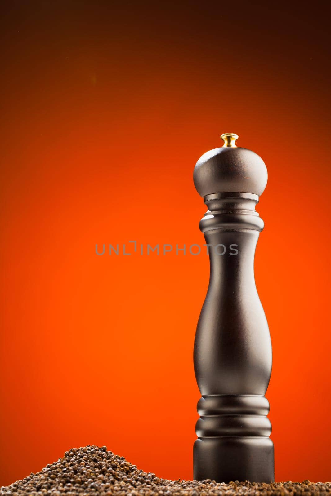 pepper mill and peppercorns heap, orange background by nikkytok