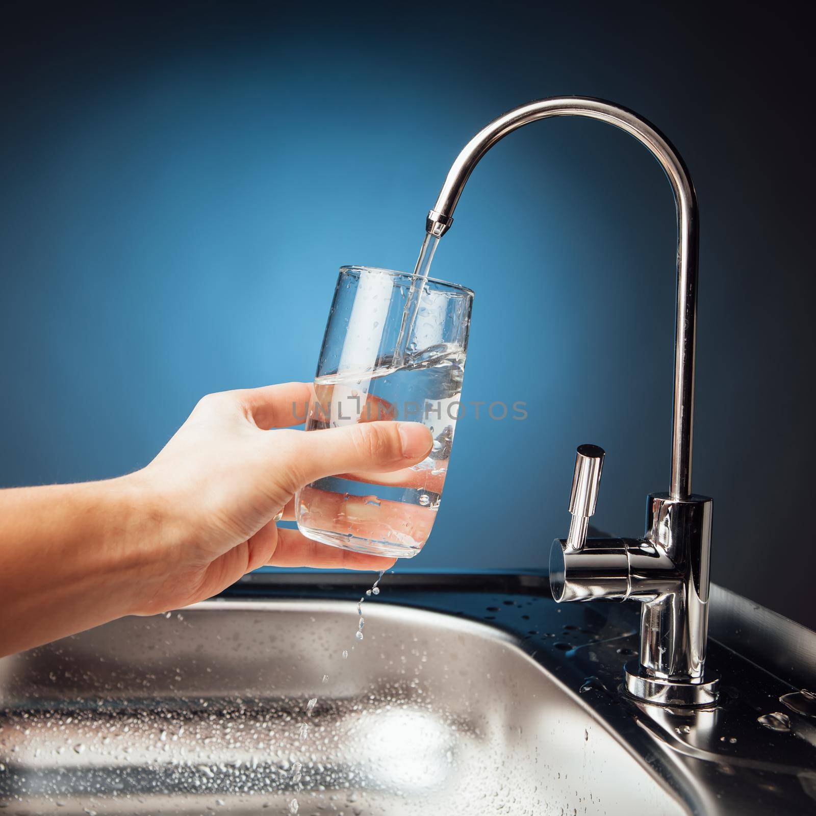 hand pouring a glass of water from filter tap, blue background