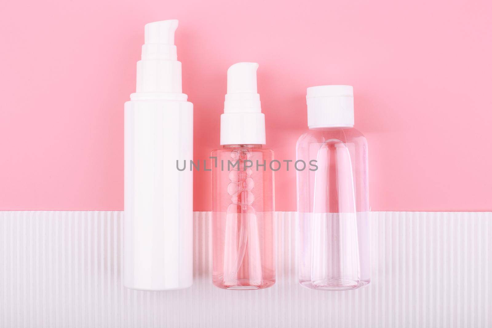 Top view of set of cosmetic tubes against pink background and white paper with stripes. Concept of skin care and beauty