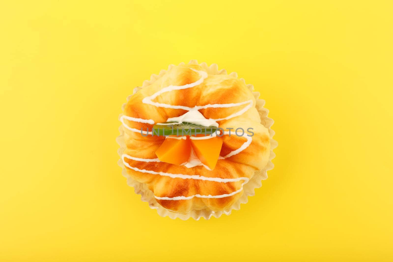 Top view of cupcake with pieces of peaches and kiwi fruit and cream against yellow background. Creative concept of desserts and sweet food