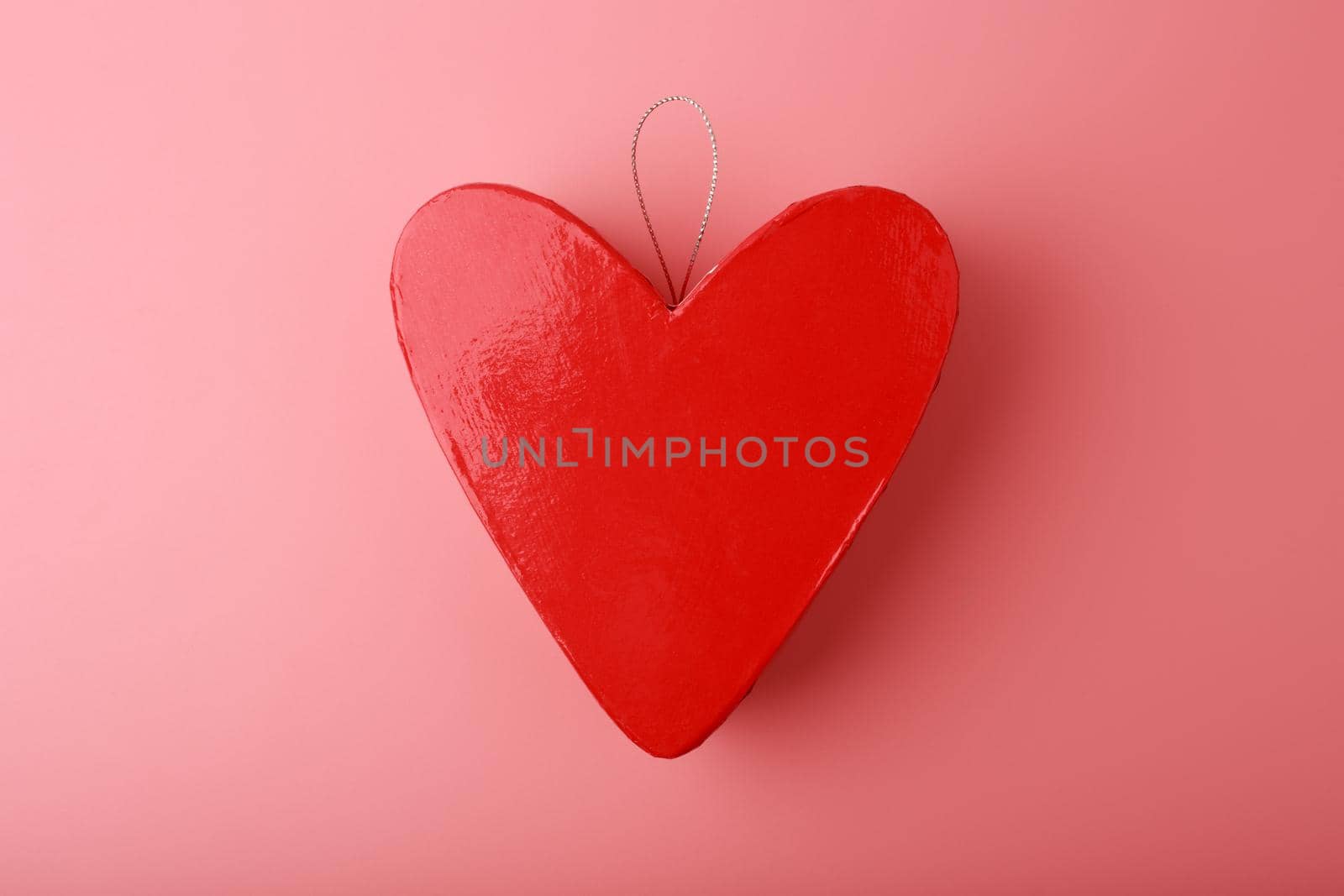 Top view of red glossy heart shaped gift box against pink background. Concept of love and togetherness