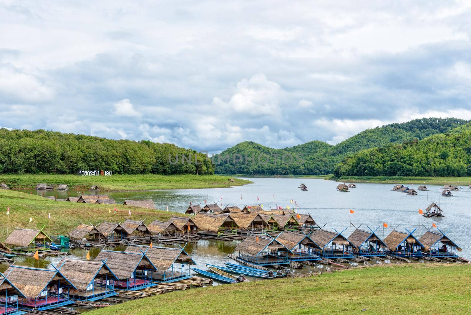 Nameplate of Huai Krathing at Loei on the grassy hill and bamboo raft shelter are floating restaurant in the middle of water under the blue sky as a tourist attraction in Thailand